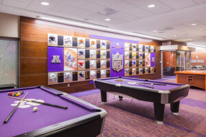 Room with two purple pool tables, NFL-themed wall with helmets, and glass cabinet displayed inside.