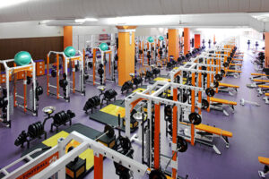 A spacious gym with rows of weightlifting equipment, benches, and exercise machines on a purple floor.