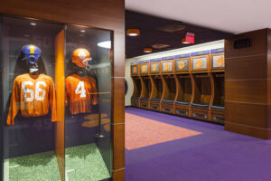 Football locker room with a display case showing two vintage football uniforms and helmets on the left.