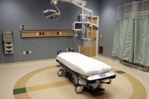 Hospital room with a surgical bed, overhead lights, medical equipment, and curtains on the right side.