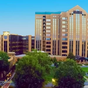 Aerial view of a large office building complex surrounded by trees, with a clear blue sky in the background.