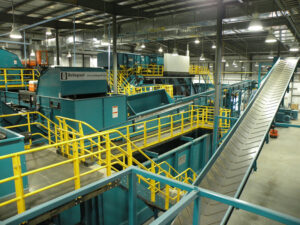 Interior view of a recycling plant with conveyor belts, machinery, and safety railings.