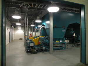 Industrial machinery in a well-lit room with overhead lighting and a cement floor.