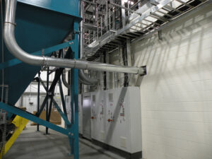 Industrial machinery and control panels in a factory setting with metal pipes and a large blue structure.