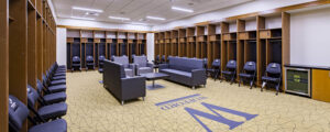 Locker room with blue cushioned chairs, gray sofas, and wooden lockers. Carpet features a large "M" and the word "Montford.