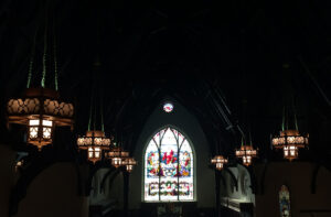 Dimly lit church interior with stained glass windows and hanging lanterns.