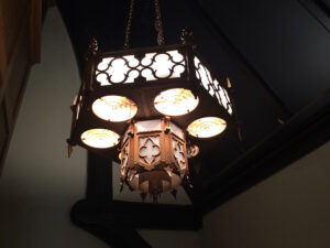 Ornate square chandelier with circular light fixtures hanging from a dark ceiling.