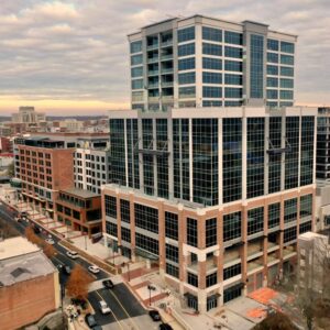 Aerial view of a modern, multi-story office building with glass windows in an urban setting under a cloudy sky.