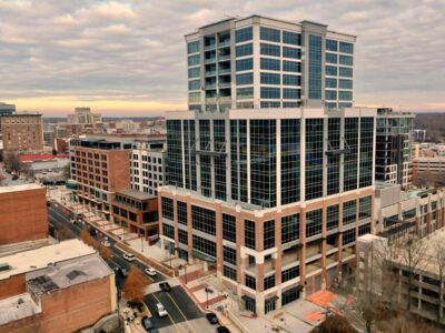 Aerial view of a modern, multi-story office building with glass windows in an urban setting under a cloudy sky.