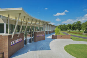 Clemson University football facility with modern architecture, featuring large windows and a curved roof, under a clear blue sky.