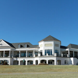 Exterior view of a large, white building with multiple balconies and a landscaped lawn under a clear blue sky.