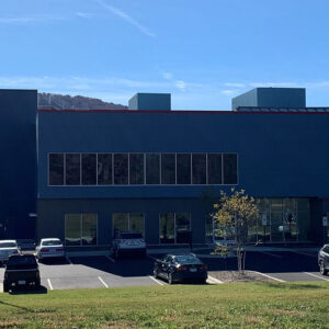 A modern building with large windows and a parking lot with several parked cars under a clear blue sky.