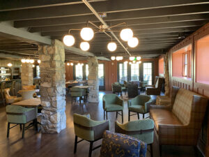 A cozy cafe interior with stone pillars, modern light fixtures, green chairs, and seating areas.