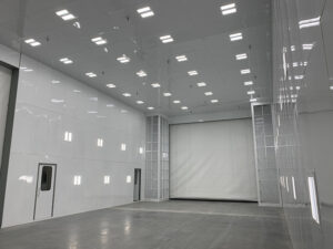 A large, empty room with polished white walls and ceiling lights, featuring a large door and ventilation panels.