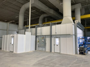 Industrial room with white walls, large ventilation pipes, control panel, and equipment in a warehouse environment.