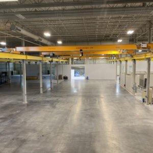 Empty industrial warehouse with yellow overhead crane and gray concrete floor.