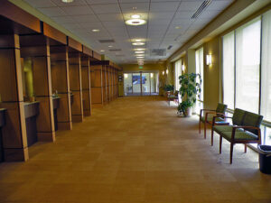 A spacious hallway with wooden partitions, chairs, and large windows letting in natural light. A door is visible at the far end.