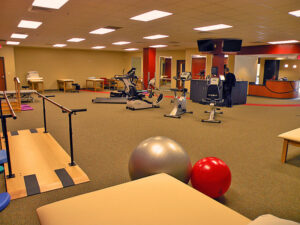 Spacious gym with exercise equipment, stability balls, parallel bars, and a reception desk in the background.