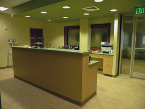 Medical reception area with an empty front desk, scale, and office equipment under fluorescent lighting.