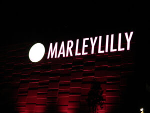 Illuminated sign with "MARLEYLILLY" in bold letters on a dark, patterned building facade at night.