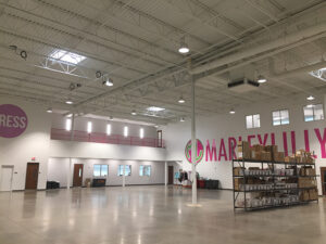 Spacious industrial interior with high ceilings, large wall signage, storage shelves, and windows.