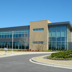 Modern two-story office building with large glass windows and landscaped surroundings under a clear blue sky.