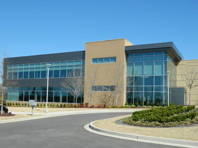 Modern two-story office building with large glass windows and landscaped surroundings under a clear blue sky.