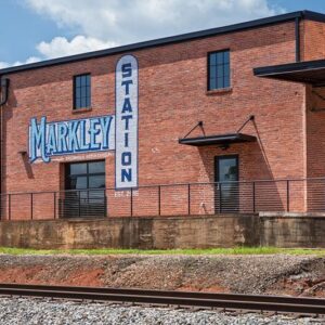 Brick building labeled "Markley Station" with large windows, next to a railway track, under a blue sky.