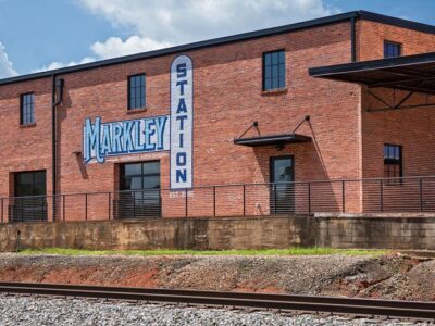 Brick building labeled "Markley Station" with large windows, next to a railway track, under a blue sky.