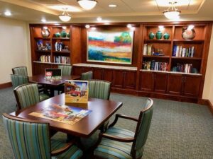 A room with tables, chairs, a large colorful painting, and bookshelves in the background, featuring puzzles and books.