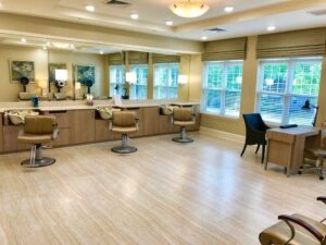 A well-lit beauty salon with four styling chairs, mirrors, vanity stations, ceiling lights, and large windows.