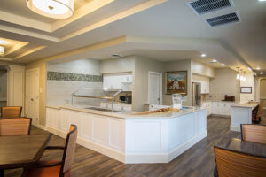 Modern kitchen with white cabinets, a kitchen island, wood flooring, and dining area with wooden chairs and tables.