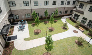 Aerial view of a courtyard with pathways, young trees, outdoor seating, and surrounding building walls.