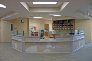 Hospital nurses' station with a modern design, featuring a curved desk, chairs, and organized shelves in the background.