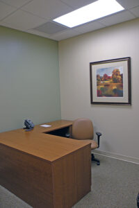 Small office with a wooden desk, brown chair, phone, and a framed landscape painting on the wall.