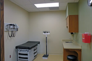 Medical examination room with an examination table, scale, and wall-mounted medical equipment.