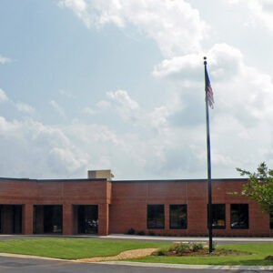 Single-story brick building with large windows, a circular driveway, and an American flag on a pole, under a partly cloudy sky.