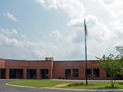 Single-story brick building with large windows, a circular driveway, and an American flag on a pole, under a partly cloudy sky.