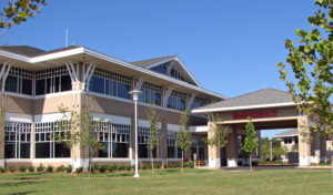 Exterior of a modern hospital building with an emergency entrance, featuring large windows and surrounded by a lawn and trees.