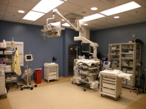 A clean, organized hospital operating room with medical equipment, storage cabinets, and overhead surgical lighting.