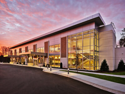 Modern building with large glass windows, surrounded by a paved driveway, against a vibrant dusk sky.