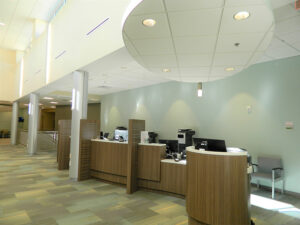 Modern, open lobby area with a row of wood-paneled service counters, computers, and chairs under ceiling lights.