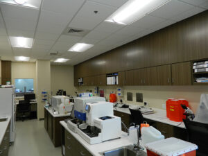 A laboratory with equipment and cabinets, featuring workstations, a sink, and storage containers on the countertops.