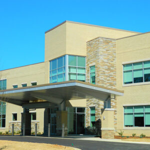 Modern two-story building with large windows and a covered entrance, set against a clear blue sky.