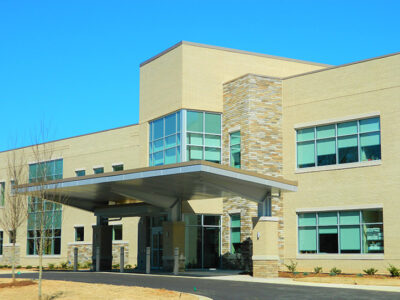 Modern two-story building with large windows and a covered entrance, set against a clear blue sky.