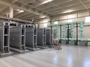 A spacious industrial room with large metal equipment and blue pipes. A red ladder is positioned nearby on the polished floor.