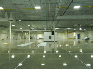 Spacious empty warehouse with polished concrete floors, white walls, and overhead lighting.