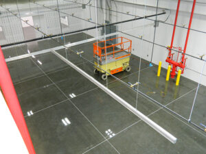 Scissor lift in an empty industrial space with polished concrete floor, red pipes, and overhead ceiling grid installation.