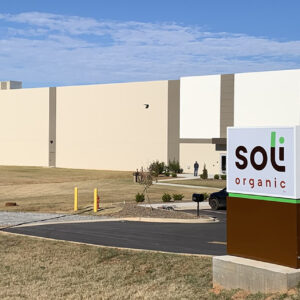 Large beige building with "soli organic" sign in front, surrounded by a grassy area and parked cars.