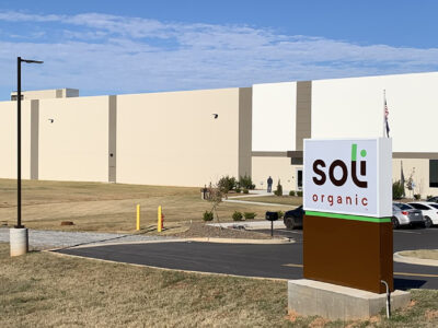 Large beige building with "soli organic" sign in front, surrounded by a grassy area and parked cars.